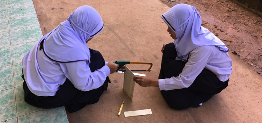 Two students sawing outside to build their prototype in Ao Kapor. 