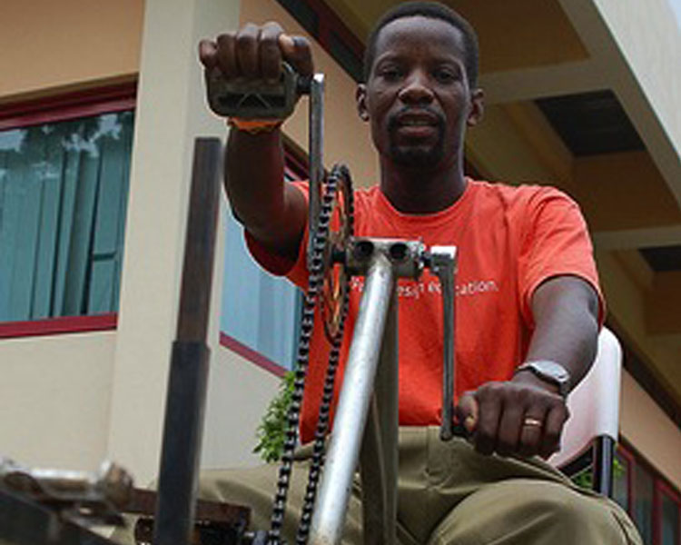 Bernard demonstrating his pedal-powered hacksaw at Maker Faire Africa in Ghana. Photo Credit: Erik Hersman