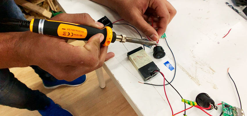 A student solders two wires together to make the circuit for his power bank.