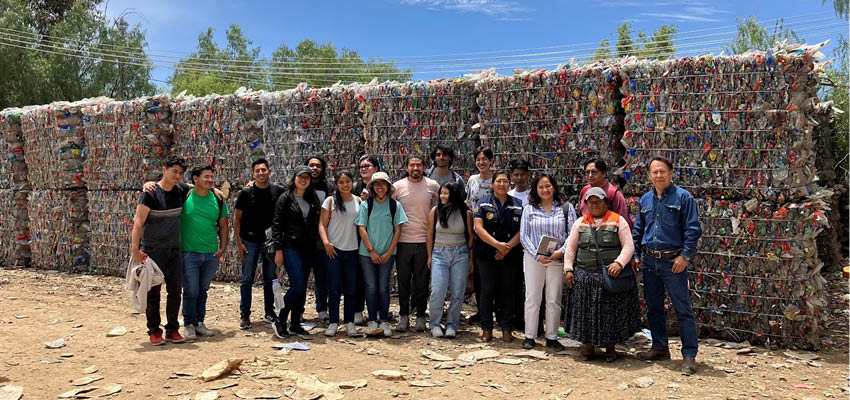 A group of 17 people standing in front of a wall of compressed trash/recyclables.