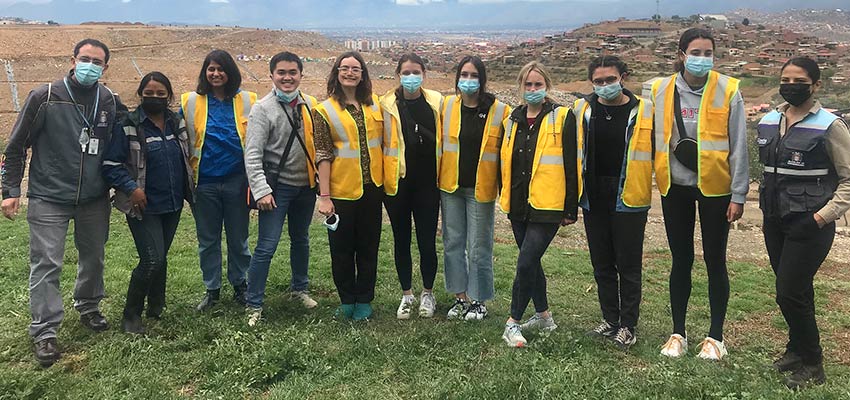11 people, several with hospital masks, standing in front of a landfill.