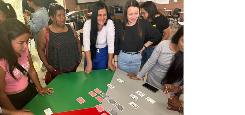 Five women standing over a table with hand made game cards on it.