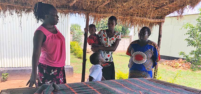 Betty Ikalny describes the brick evaporative cooling chamber and its benefits to vegetable vendors Agnes Irasu and Tabitha Ajuro.