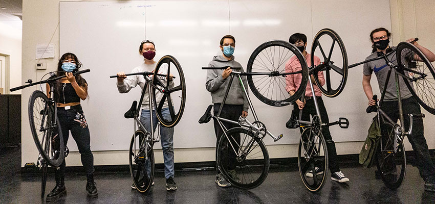 Group of five people holding up bicycles.