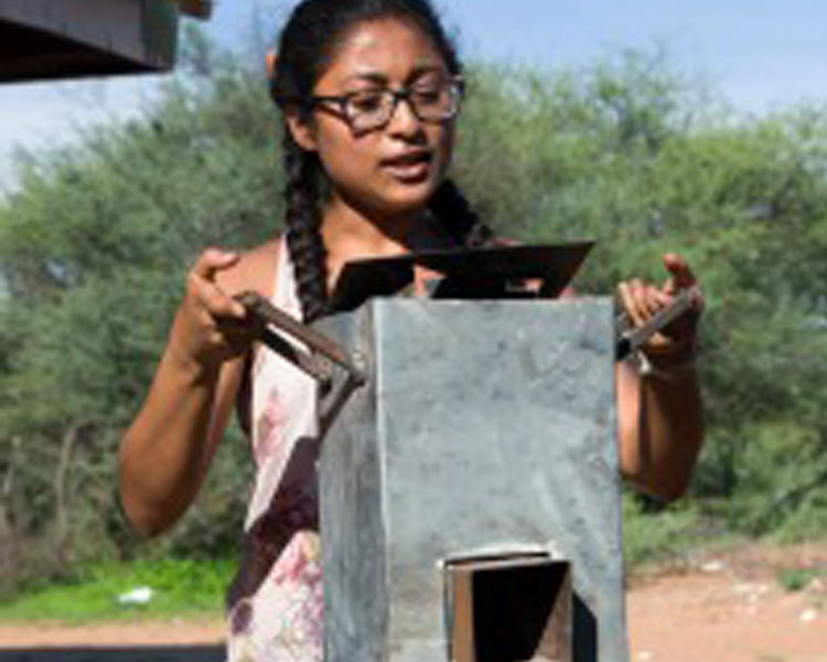 Kavya '17 explains the merits of a small rocket stove design.