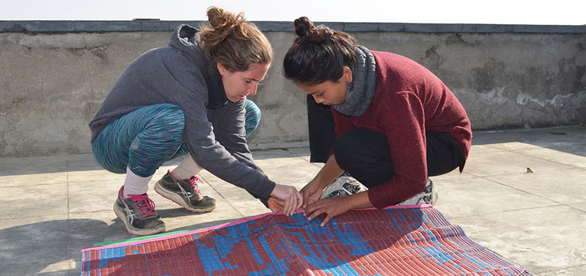 Ines and Sandhya working together to sew two chatai mats together on the roof of the Solambu Hospital Center.