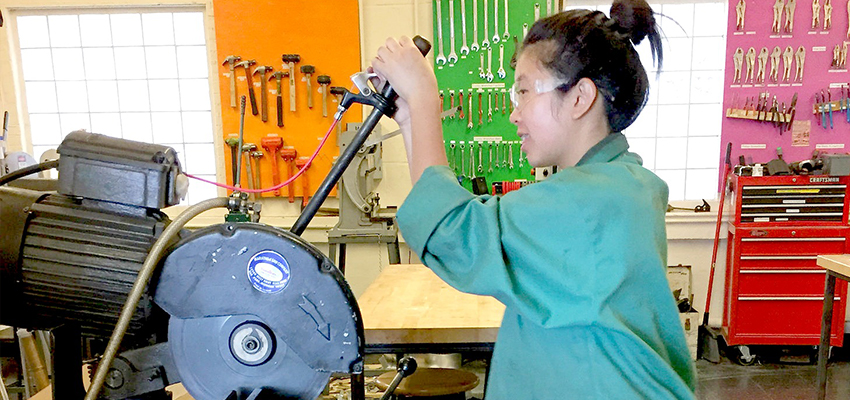 D-Lab: Design student cutting steel in the D-Lab workshop.