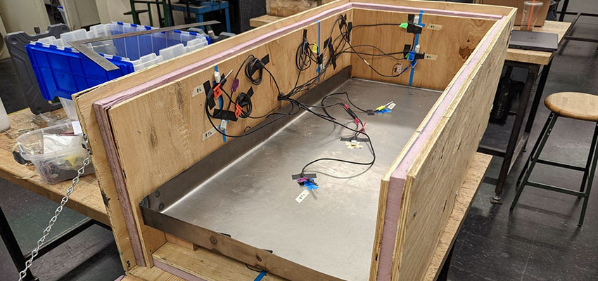 The photo above shows the current quarter-size brooder box. It is made from wood and foam insulation with an elevated metal tray for the chicks to stand on above a compartment for phase change materials (paraffin wax) to heat the space). Temperature sensors are placed inside the box to measure the temperature and humidity over time. Photo: Courtesy MIT D-Lab