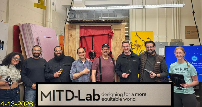 A group of eight smiling men and women standing in a line in a workshop.