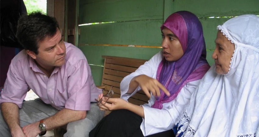 A man seated at left in conversation with two women seated at right.