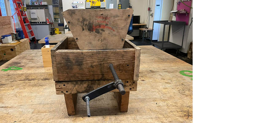 A wooden box with a metal arm on a work table.