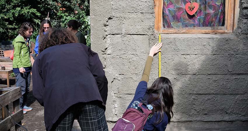 A woman crouching in front of a cinderblock structure, measuring the wall.