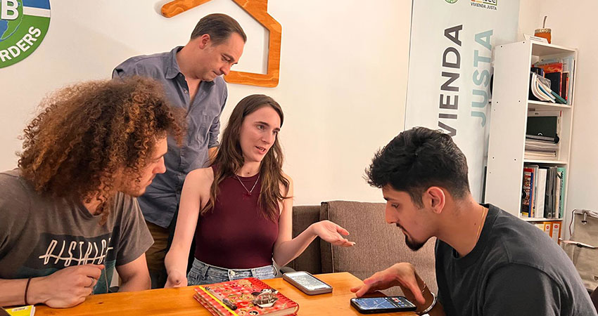 Three people having a discussion over a a table with one person standing nearby.