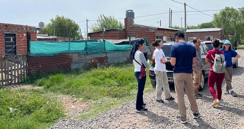 Six people standing at right on a pebbled road.