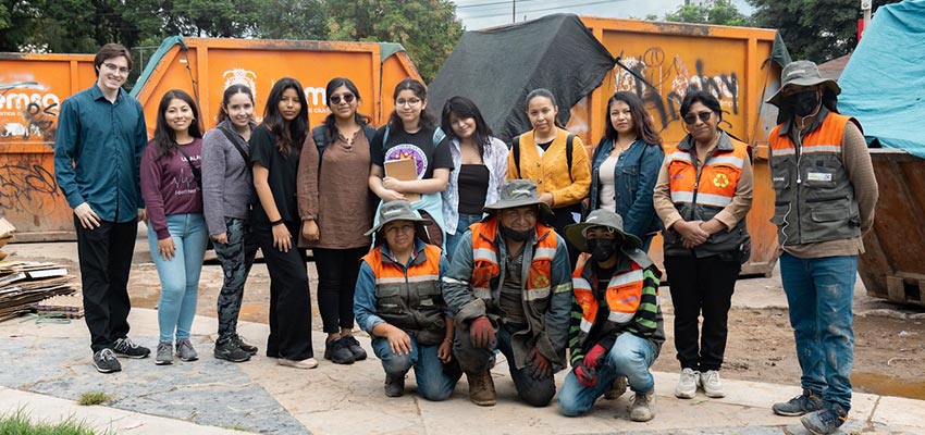 A group of about a dozen people standing in front of orange dumpsters.