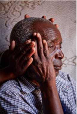 A close-up of an older man holding one hand to the side of his face; two other hands hover around the back and side of his head.