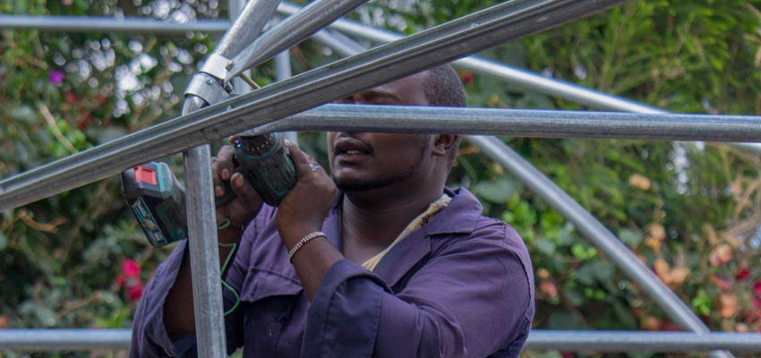 Man standng inside a large metal frame, working on a joint.
