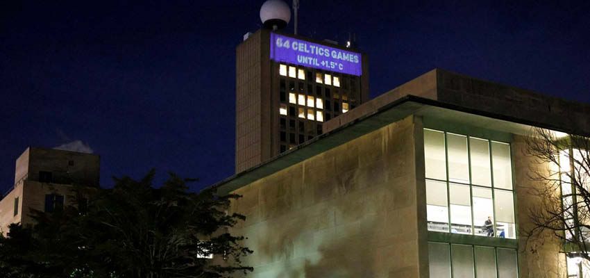 Building at night, lit from within with a "climate clock" projected on the taller building at rear.