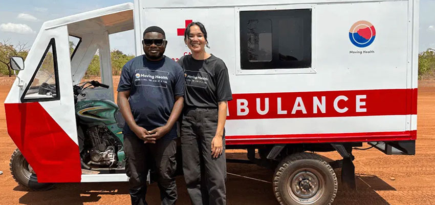 A man and a woman standing by a three wheeled ambulance.