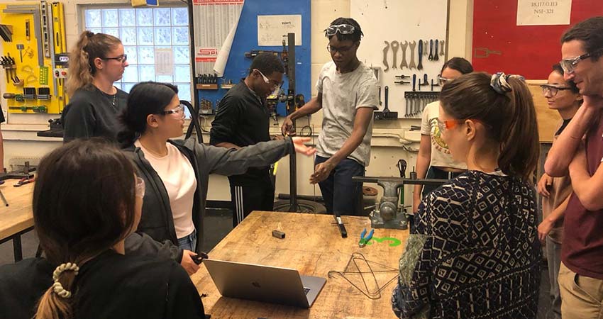 Half dozen university students gathered around a workshop table.