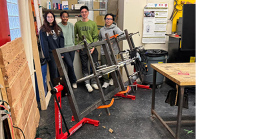 Group of 4 young people standing behind a large metal structure in a workshop.