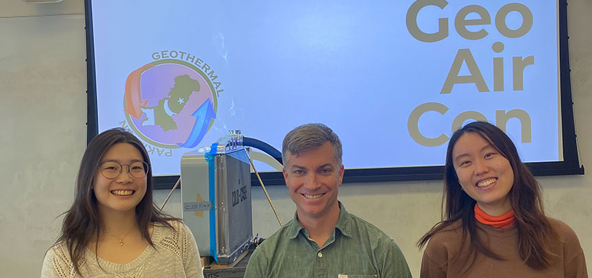 Two smiling women and a smiling man in front of a projection screen that reads Geo Air Con.