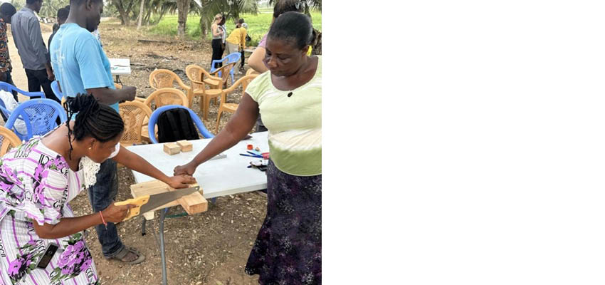 Two women at a table hand sawing a piece of wood.