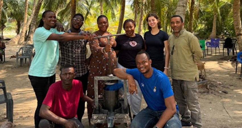 A smiling group of 6 people standing around a metal object.