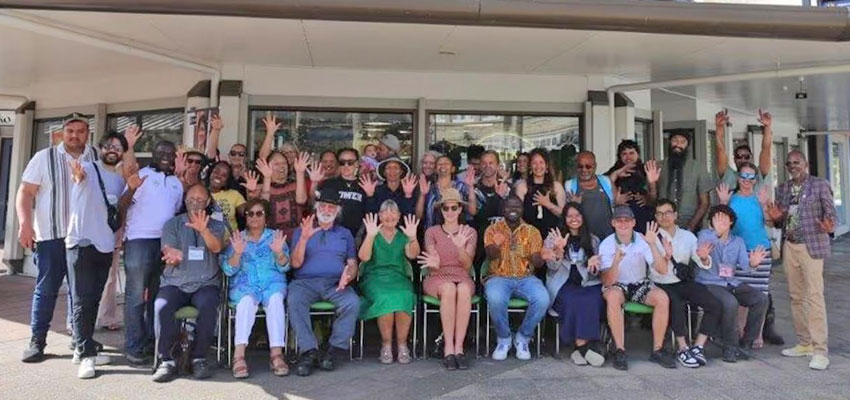 Group of more than 20 people under an outside awning posing for a picture.