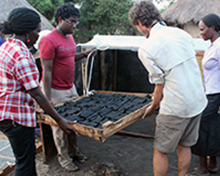 Betty tests a solar dryer for charcoal bricks with her team in Uganda. 