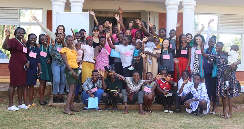 Large group of mostly women, a few holding babies, smiling and waving.