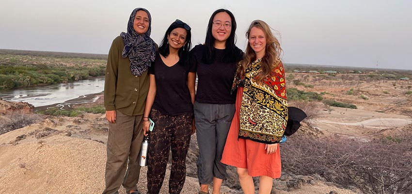 Four women standing in a rural, arid outdoor setting.