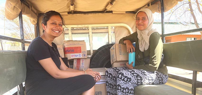 Two smiling women sitting on bench-style seats across from one another in an open-air van.