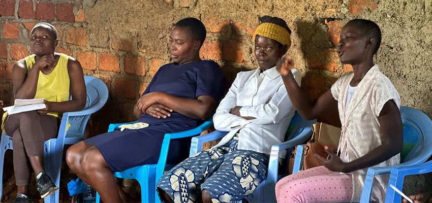 Four women seated in chairs in front of a masonry wall.