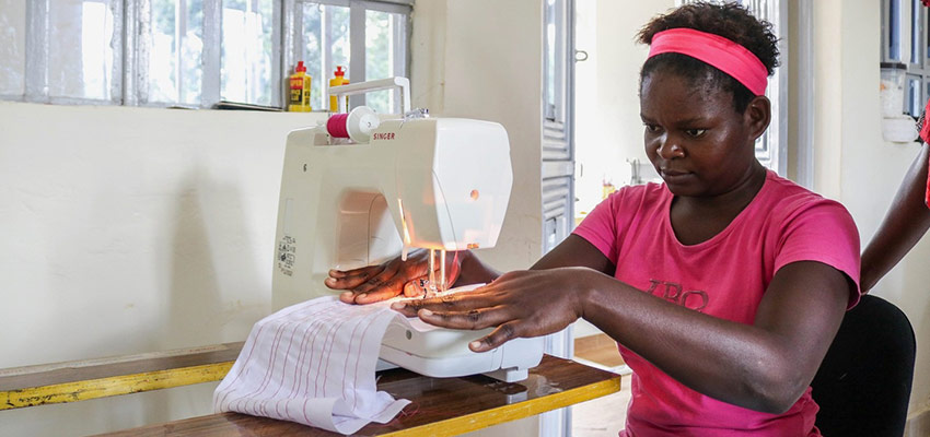 A woman in a pink -shirt seated at a table passing fabric through a sewing machine.