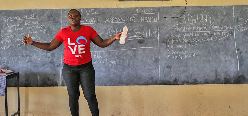 Women in red t-shirt standing with her arms out in front of chalk board.