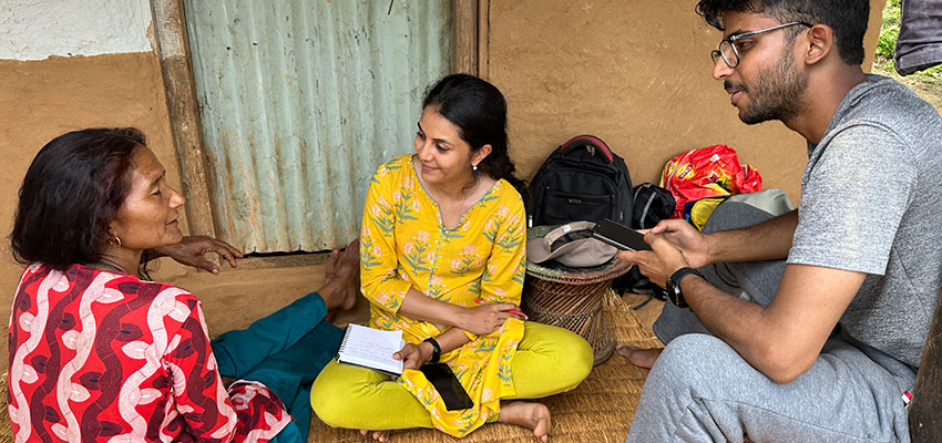 Two women seated on the floor talk to a bearded many sitting on a low chair.