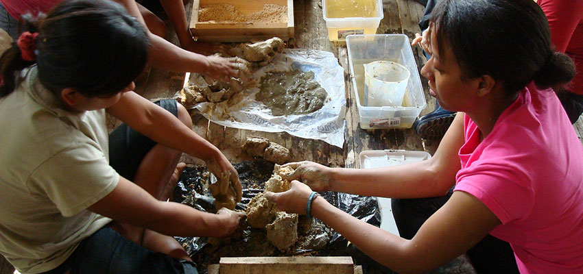 Two women seated opposite each other working with wet clay.