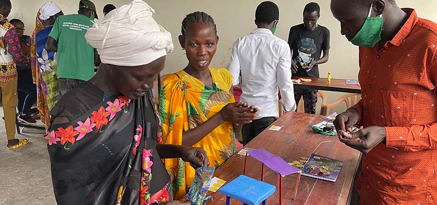 Three women standing at a table constructing small models from paper and pipe cleaners.