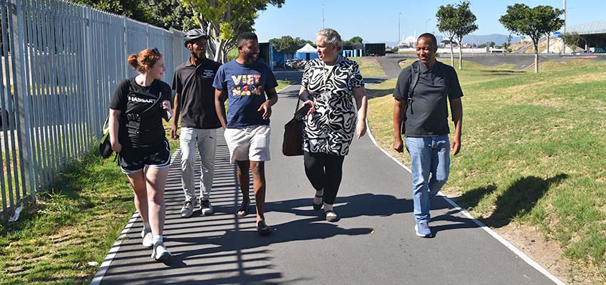 Five people walking in a row towards the camera on a paved path.