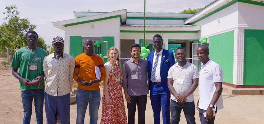 Nine people standing in front of a one-story bright green and white building.