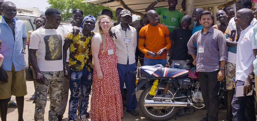 A group of smiling people stanind around a motorbike.