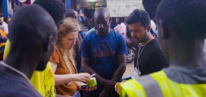 A woman standing outside holding a small object with several man standing closing around her looking.
